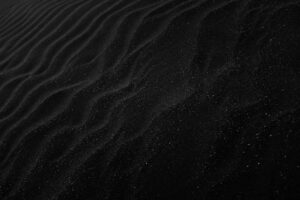 Textured black sand with ripples resembling dunes, creating a dark, abstract aesthetic.