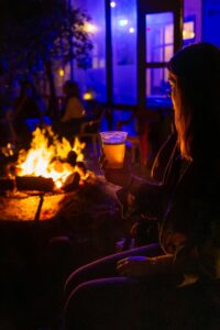 A relaxed evening by the campfire, holding a drink under colorful lights.